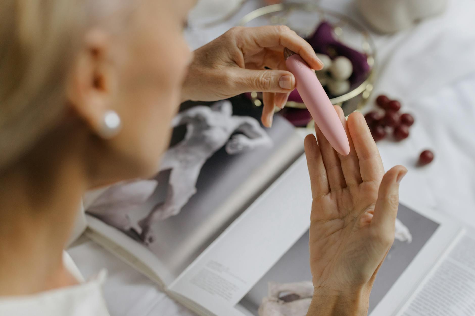 Nahaufnahme einer Frau, die einen rosa Vibrator hält, mit Kunstbüchern im Hintergrund, betont intime und persönliche Momente.